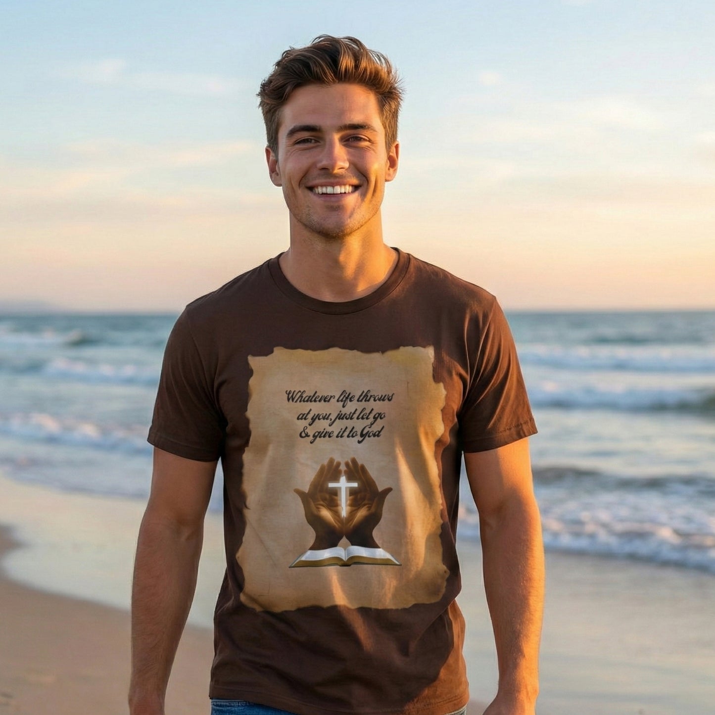 Handsome man smiling on a beach at sunset wearing a brown retro faith shirt with a parchment prayer hands design by Everyday Rebel Co.