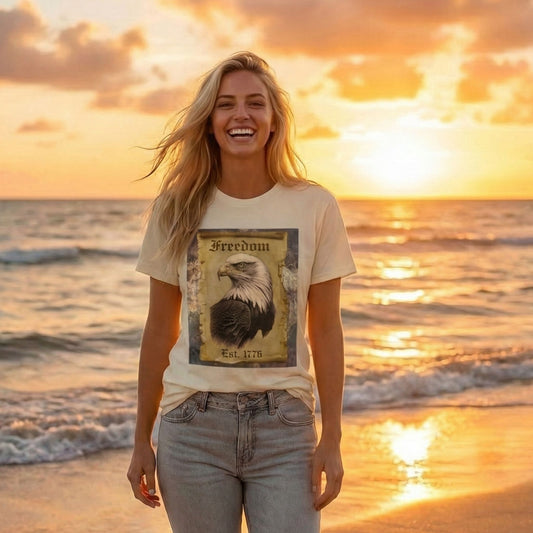 Blonde woman walking on a sunset beach wearing a cream Everyday Rebel Co. t-shirt with a vintage Freedom 1776 bald eagle design and grey rolled-up jeans.